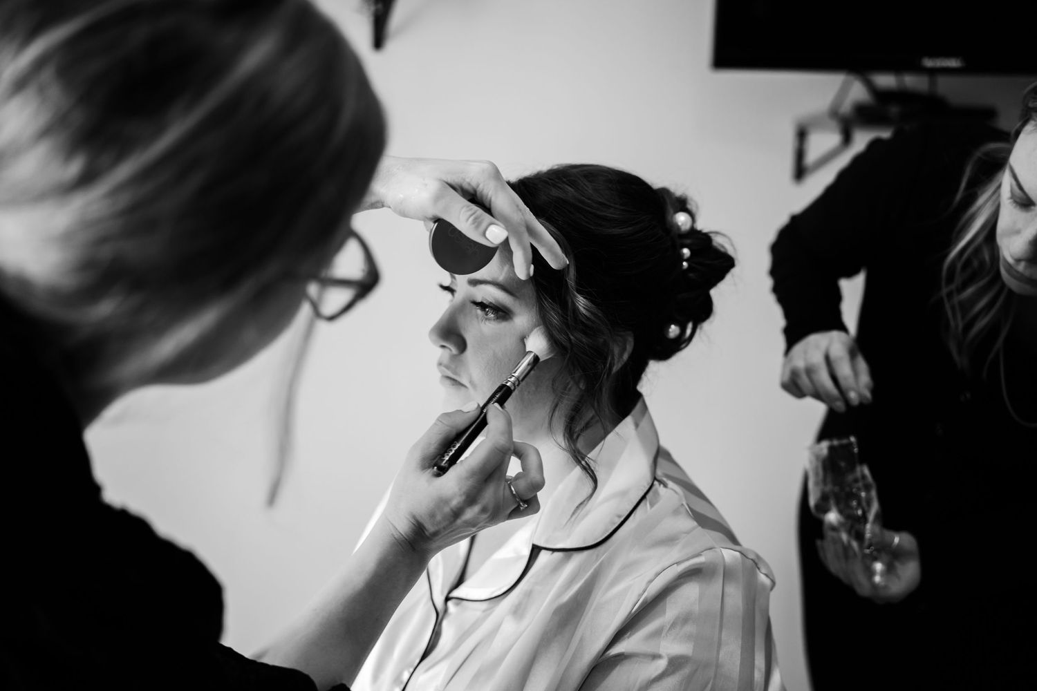 Black and white image of someone getting their makeup professionally done while wearing a light colored robe.
