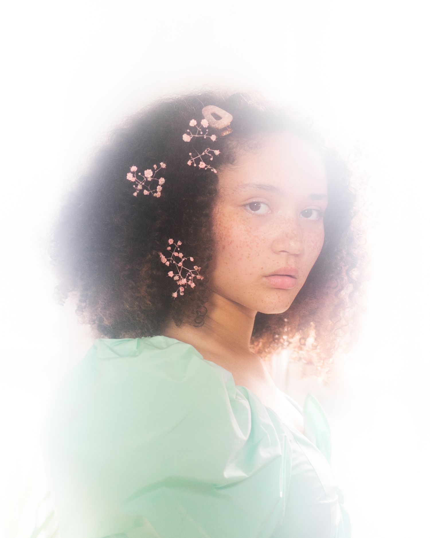 Dreamy ethereal portrait with soft lighting features delicate cherry blossoms against a mint green outfit and hazy background.