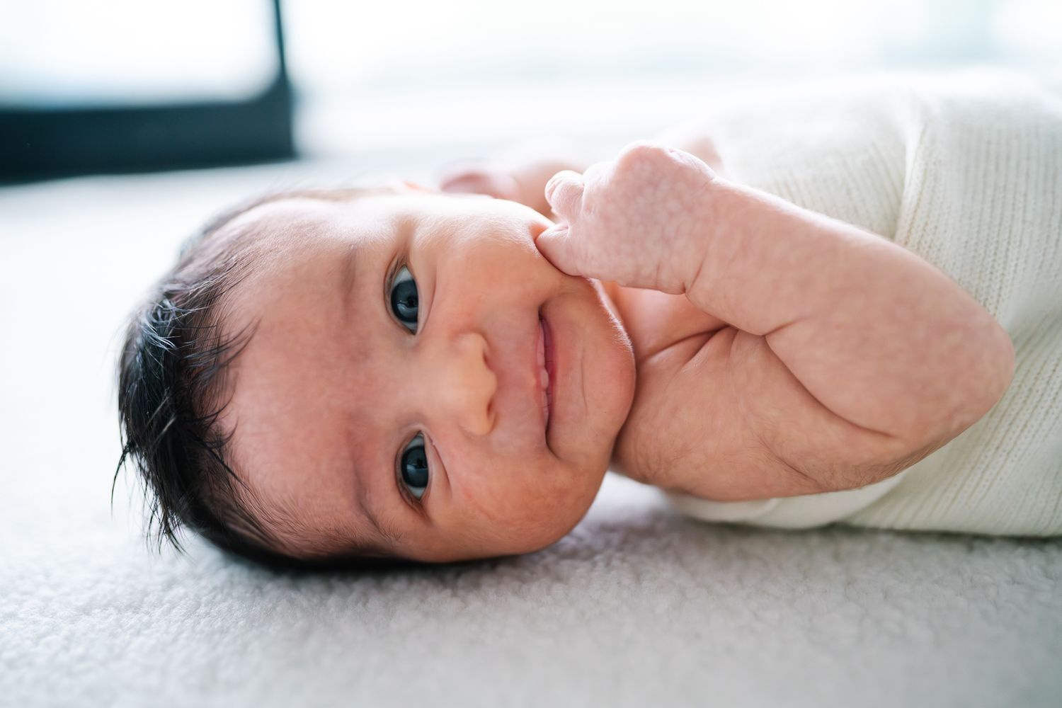 Newborn baby smiling sweetl at the camera during a newborn photoshoot at home by Melbourne newborn and family photographer Pei A Photography