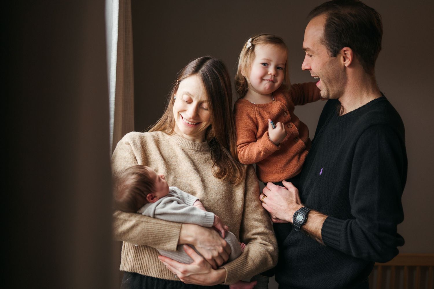 Warm family portrait by window with parents and children sharing loving moment.