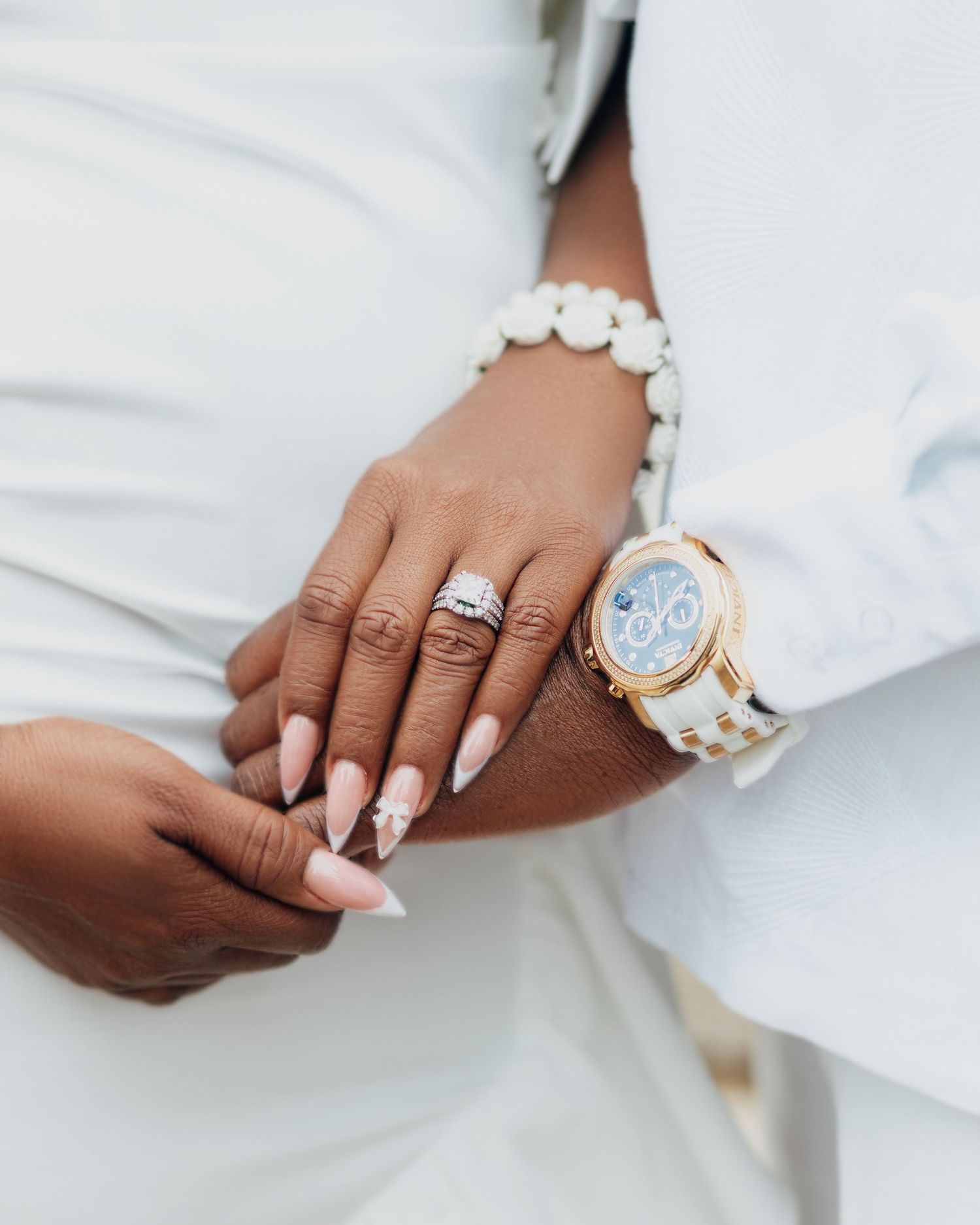 Close-up of hands wearing white manicure, engagement ring and matching white ceramic watch with gold accents.