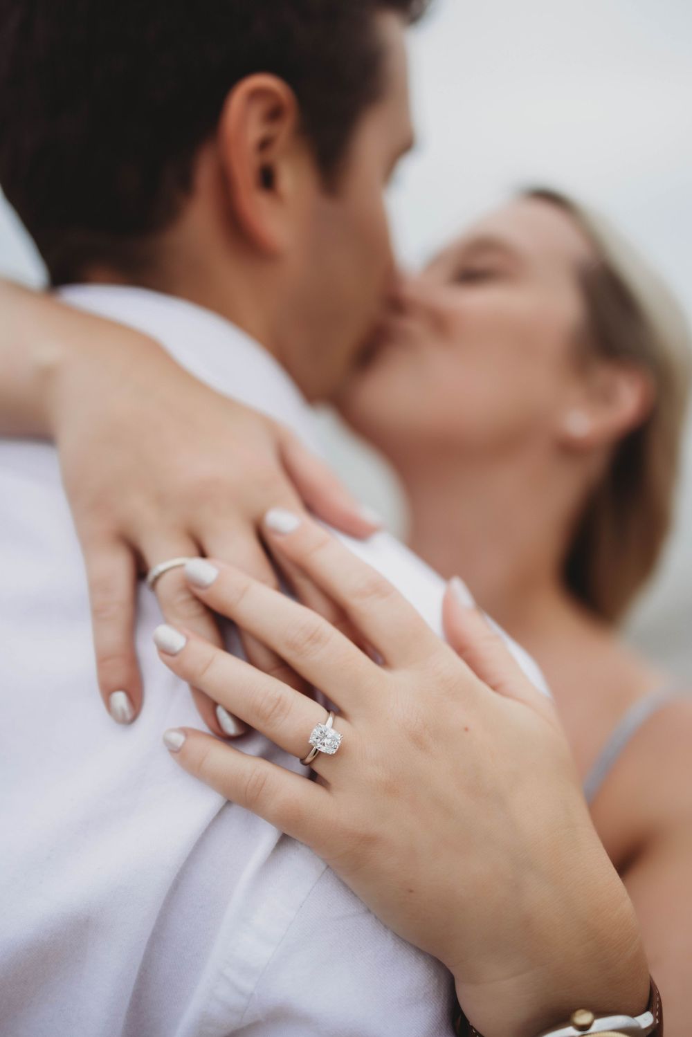 Close-up shot of a couple embracing while showing off a sparkling diamond engagement ring.