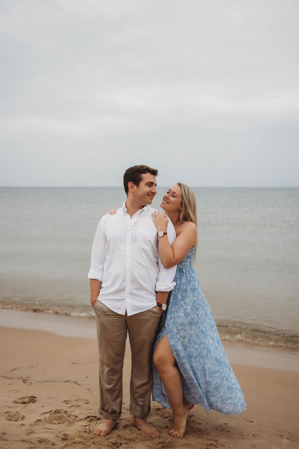 Two people sitting on a misty beach shore wearing casual dress clothes in a romantic coastal photoshoot.