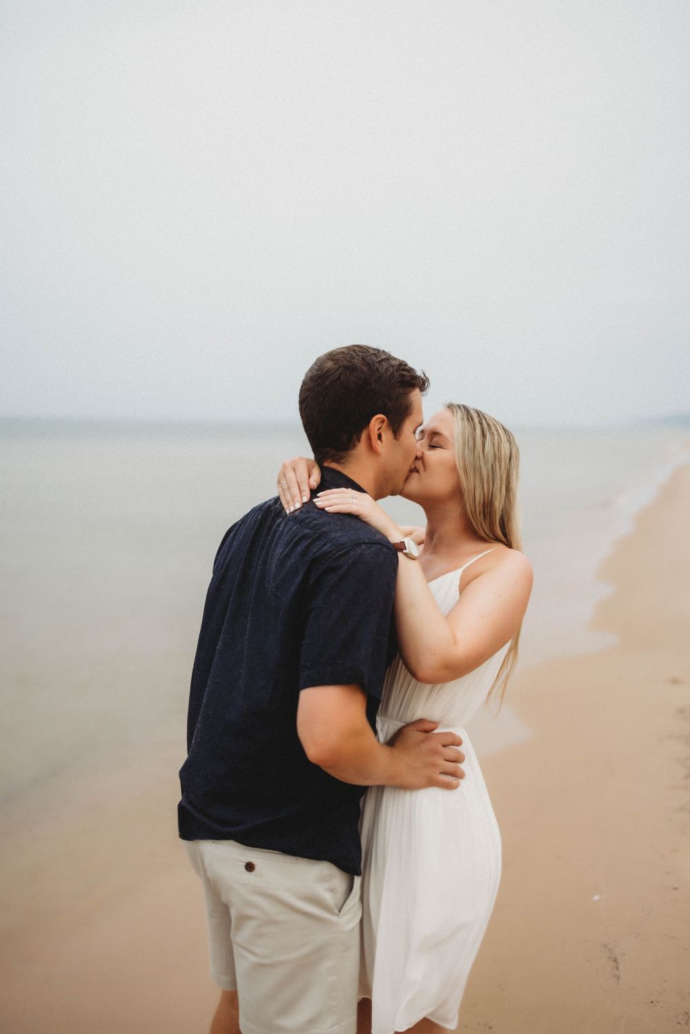 A romantic couple shares a kiss on a misty beach while wearing casual summer attire.