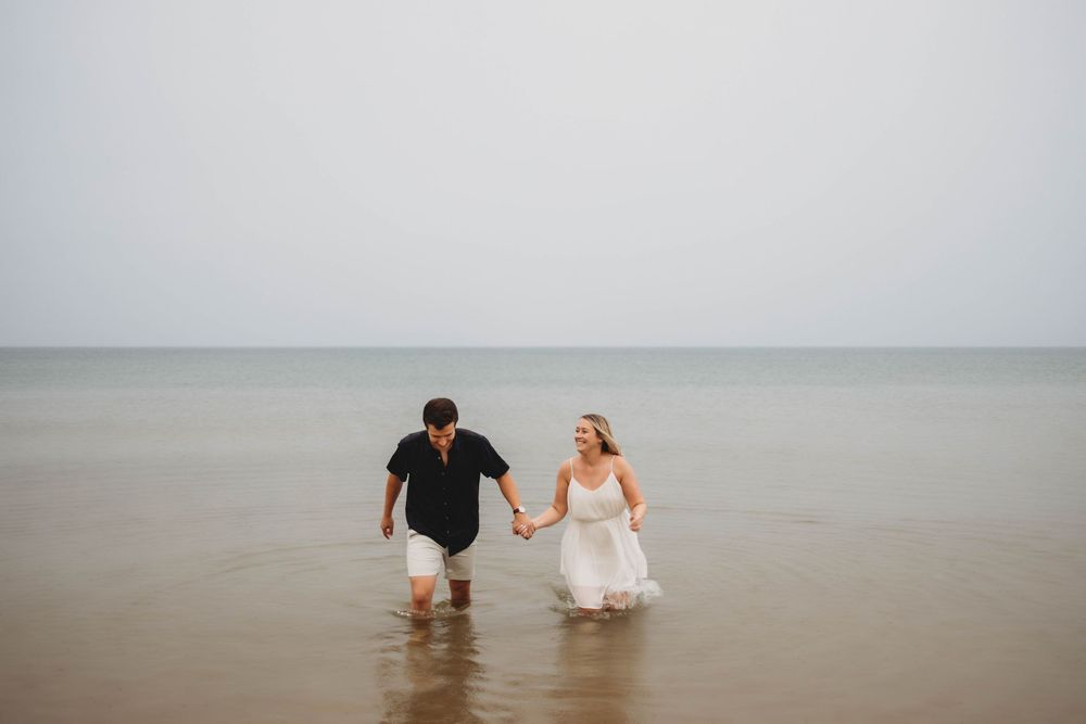 Couple holding hands while walking together in the shallow ocean water during a romantic beach photo session.