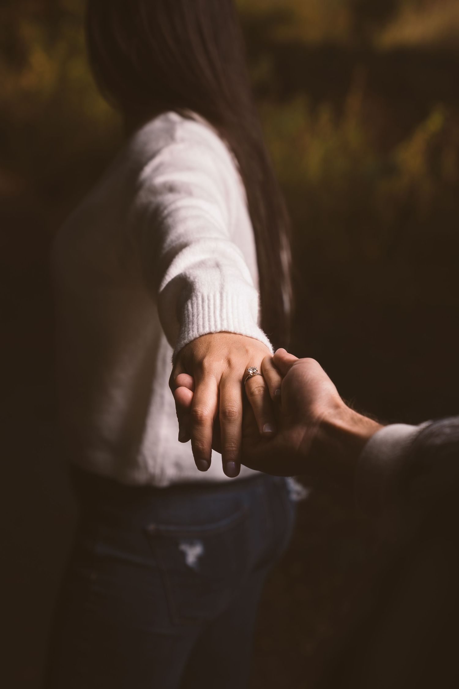 Close-up of hands holding each other against a dark autumn background.