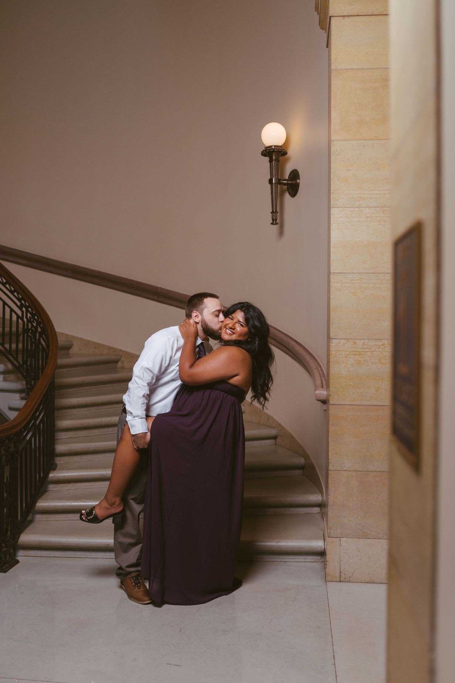 Couple sharing intimate moment on elegant staircase near wall sconce.