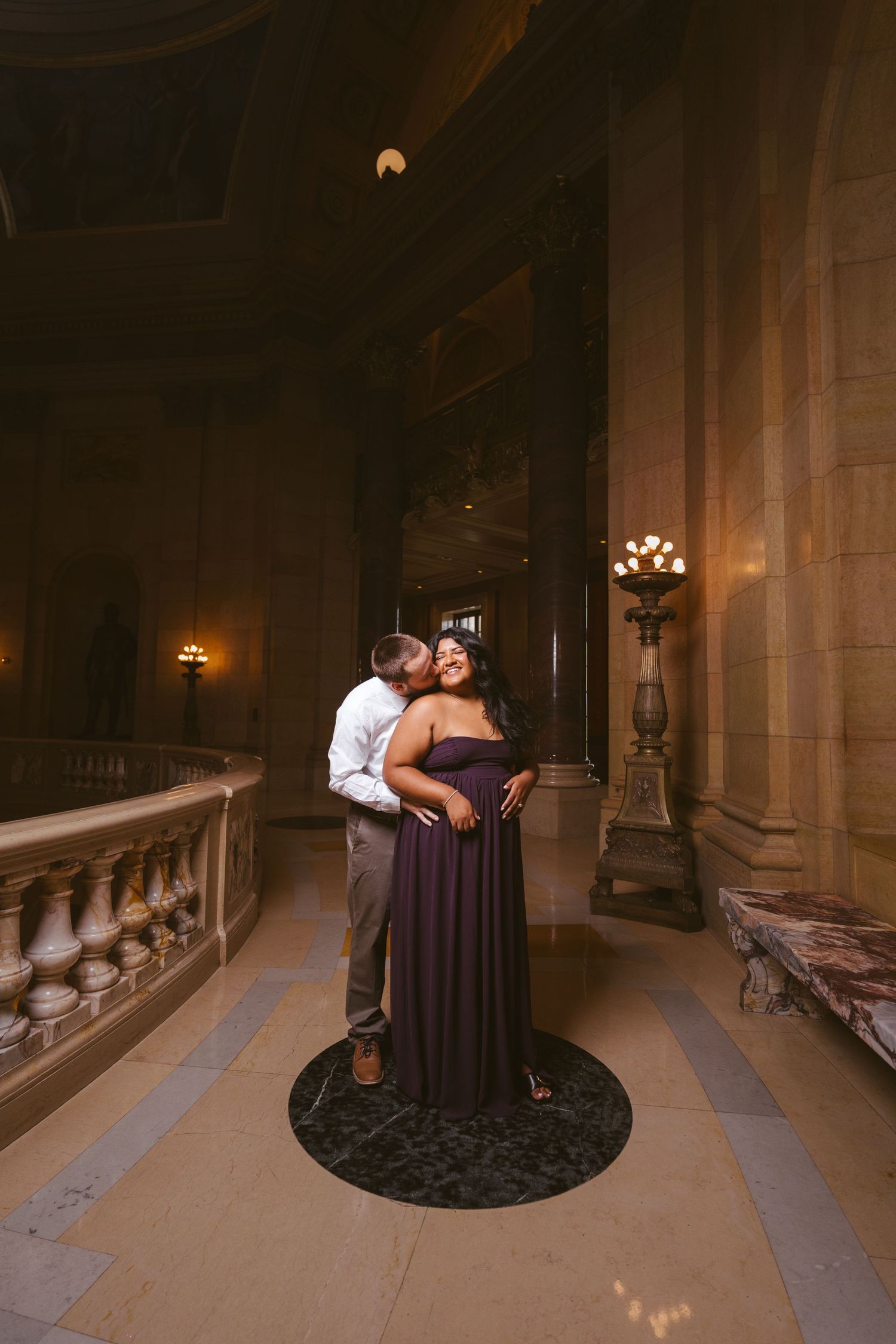 Romantic portrait of couple embracing in ornate hallway with classical architecture.