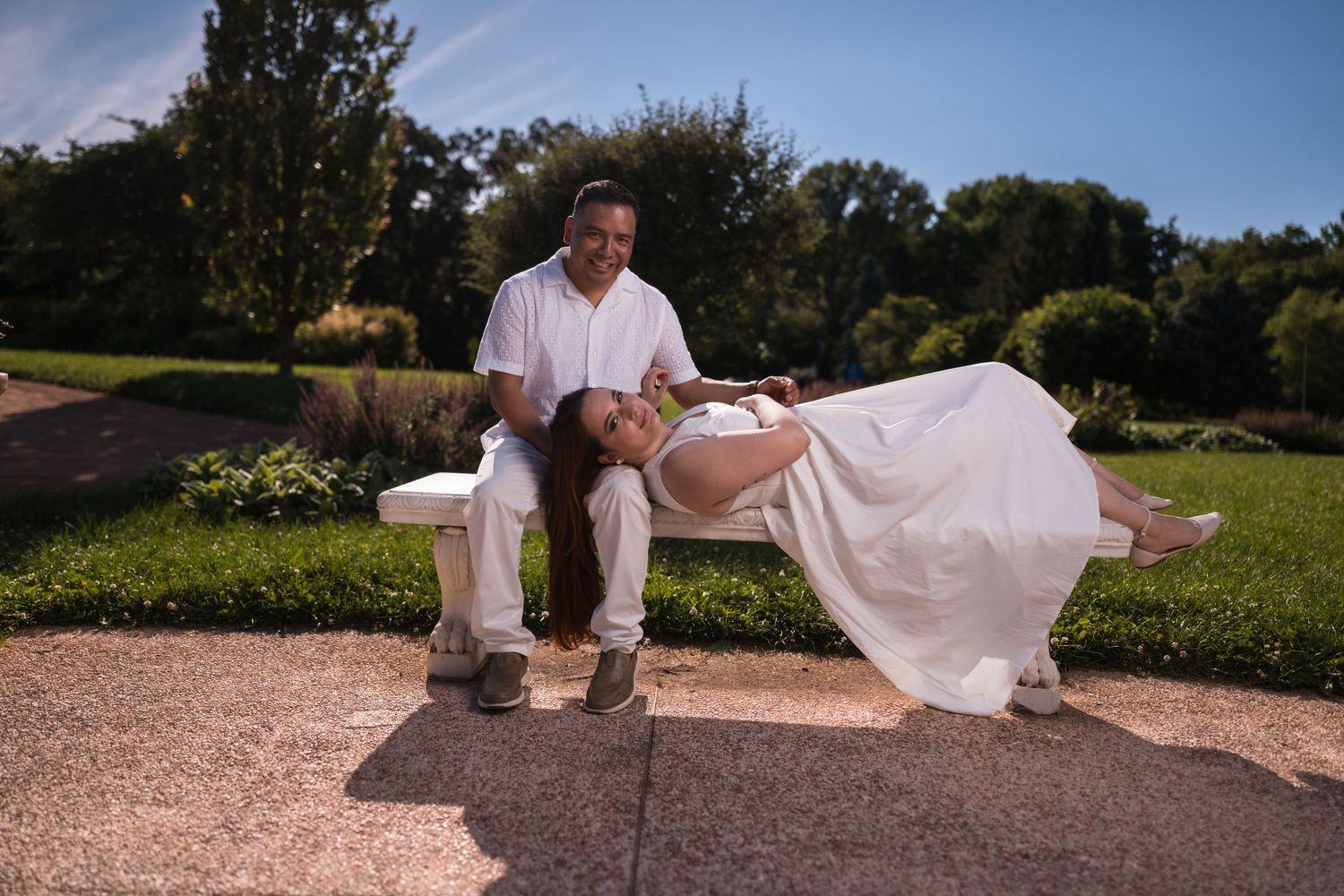 A couple in matching white outfits poses playfully during an outdoor photoshoot.