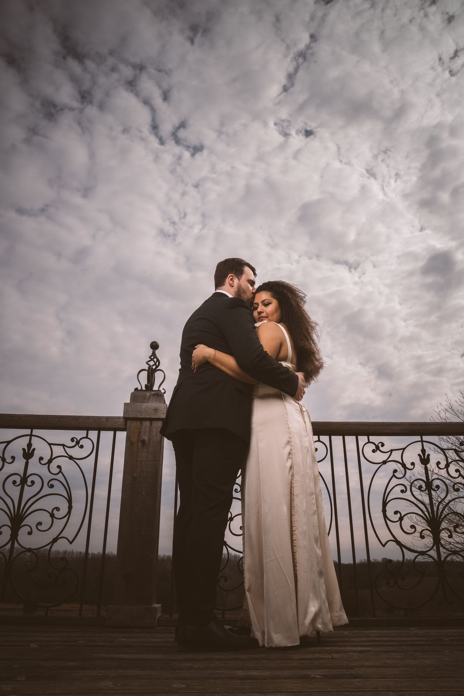 A couple shares a romantic moment on a balcony under dramatic cloudy skies.