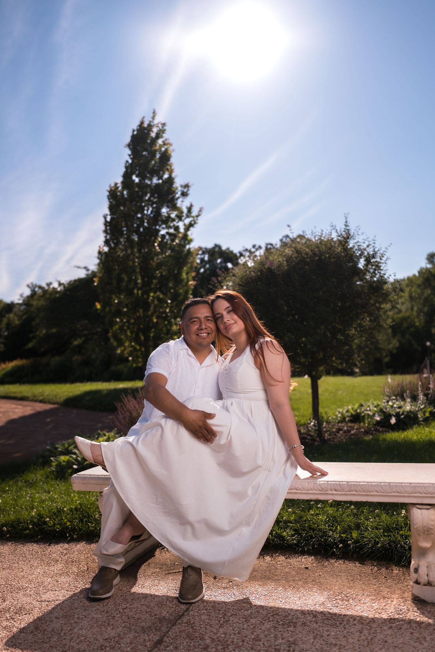 A couple shares intimate moments on a stone bench during a sunny outdoor photo session.