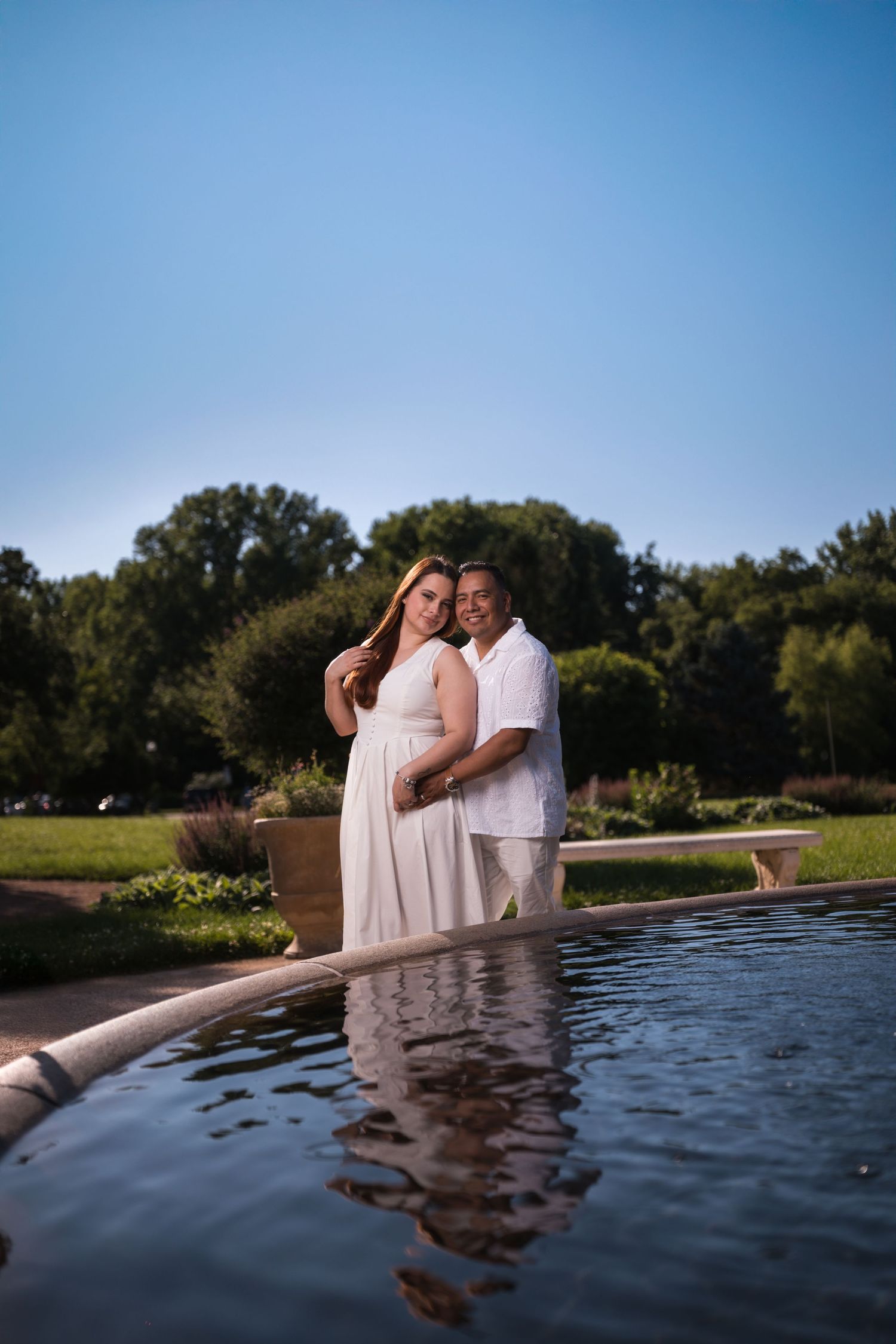 A couple in white attire shares tender moments while standing in a decorative water feature.