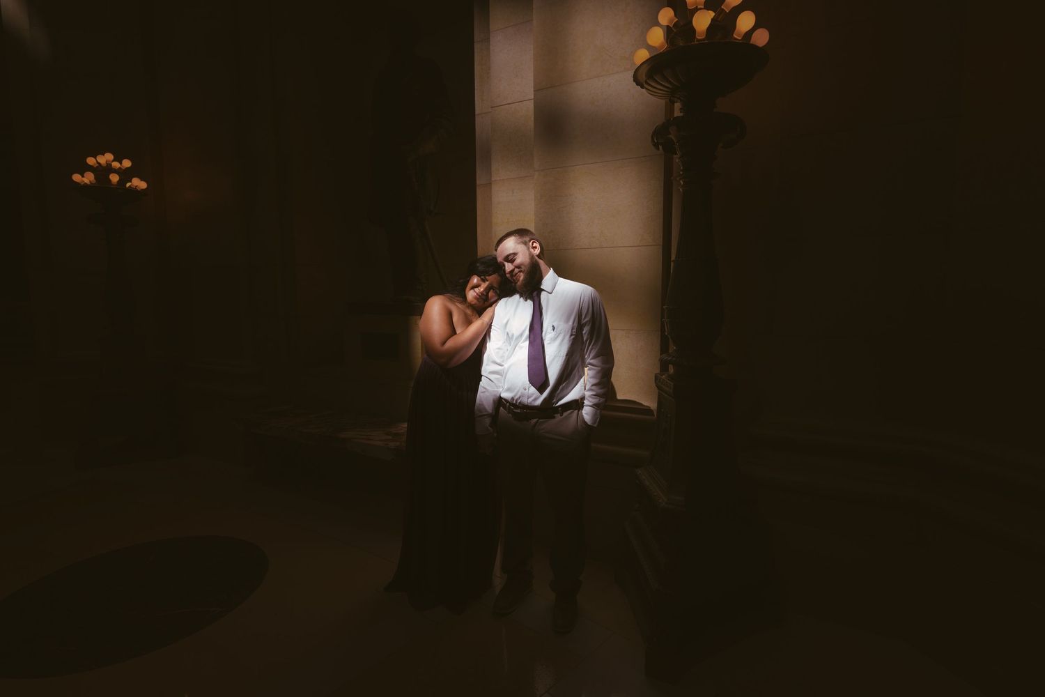 A romantic couple embraces in dramatic lighting against a dark background.