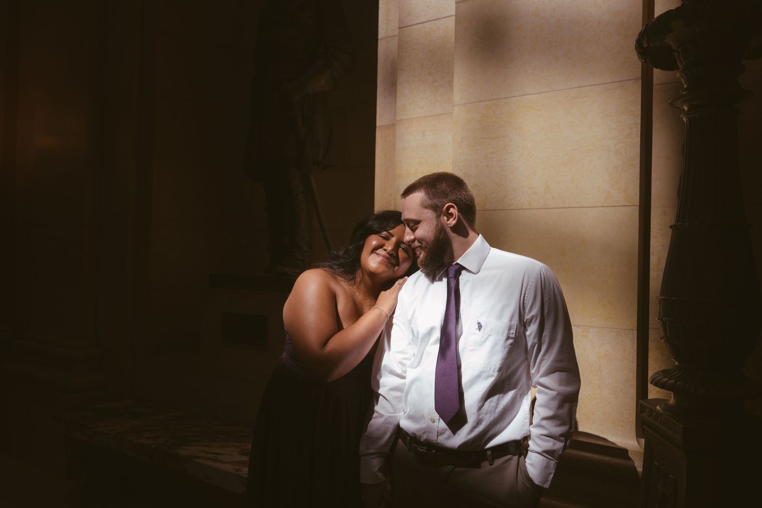 A couple shares an intimate moment in moody lighting and formal attire.