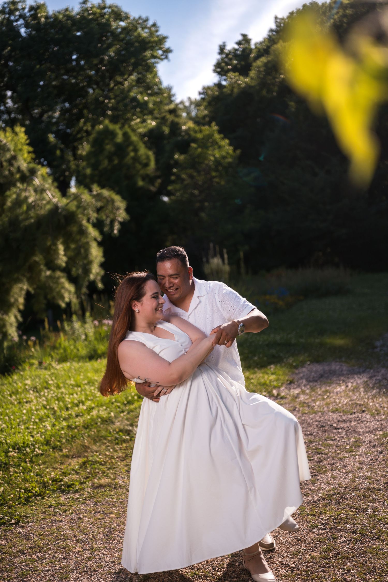 A couple in white clothing dances and embraces during an outdoor sunset photo session.