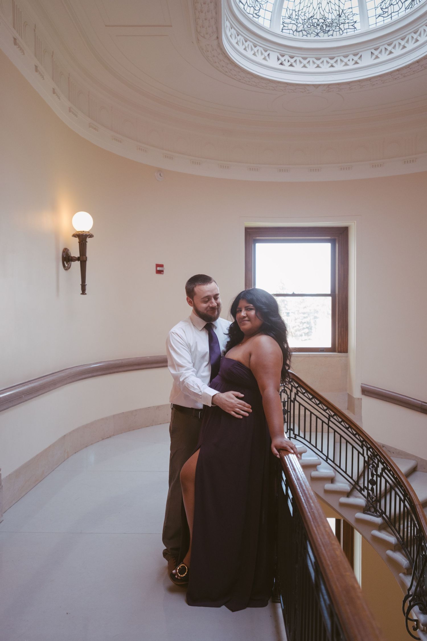 A couple embraces near a beautiful domed ceiling with decorative molding.