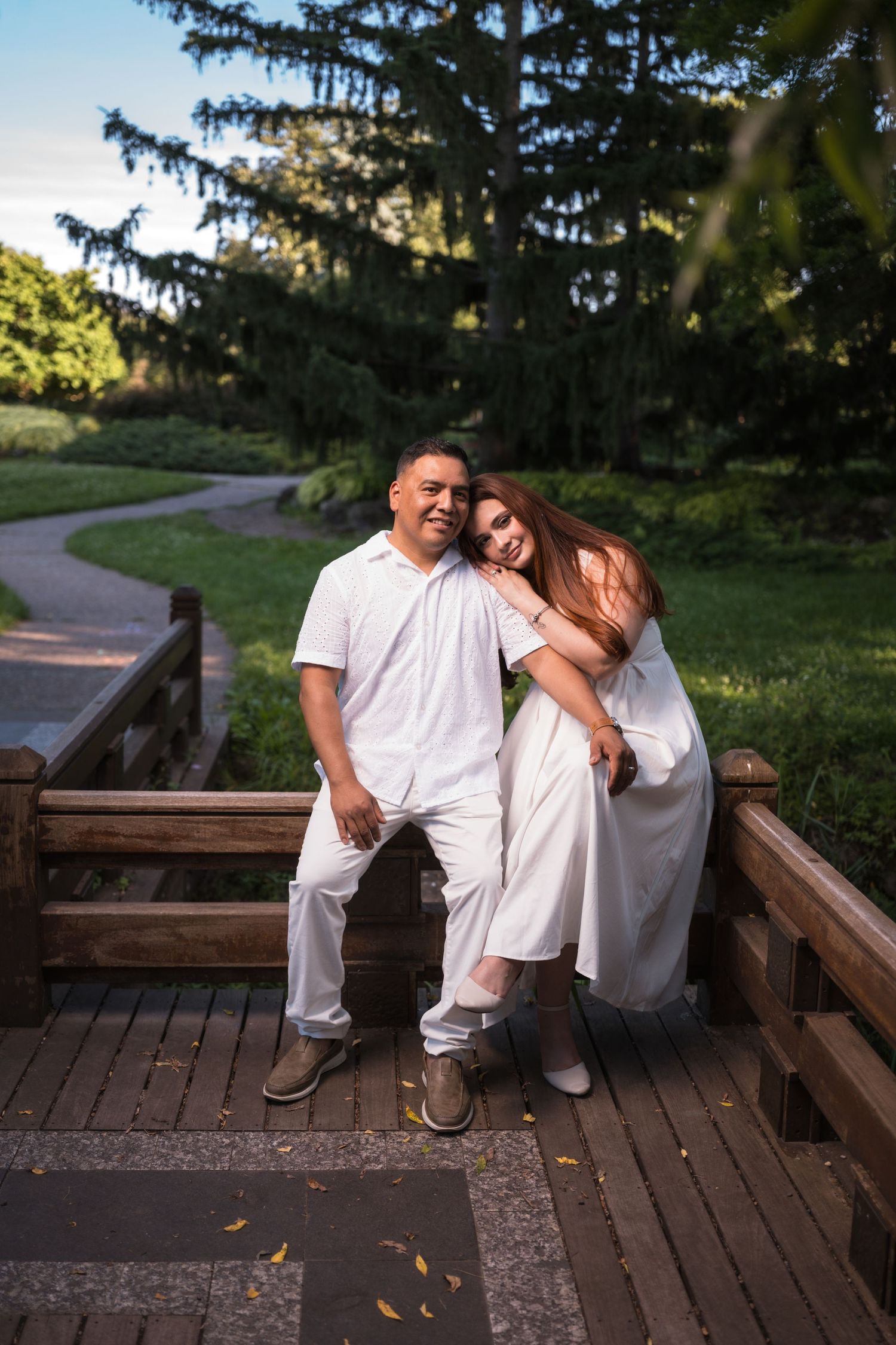 A couple shares intimate moments while sitting on a wooden deck in a park setting.
