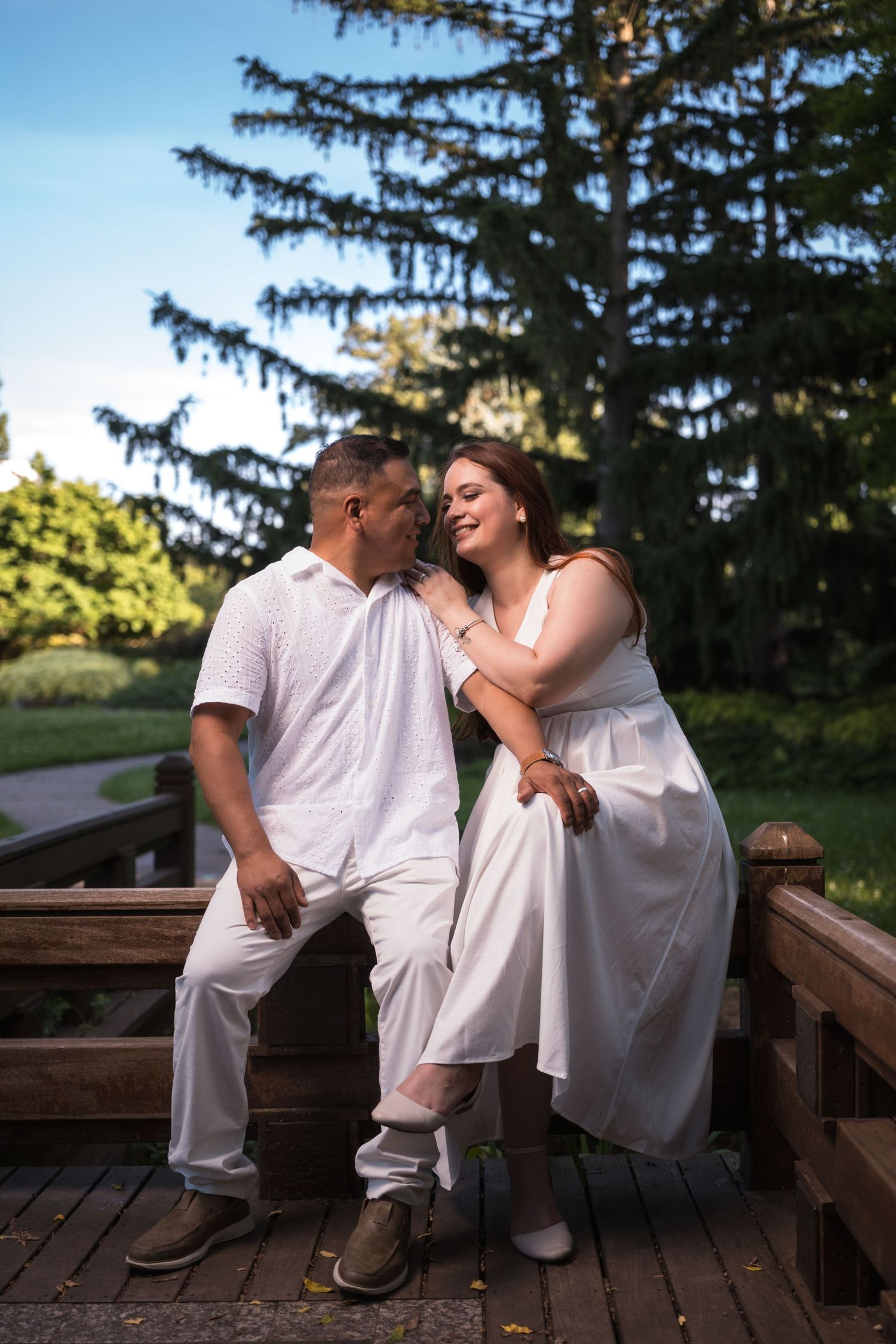 A couple laughs together while sitting on a wooden deck during a romantic photo session.