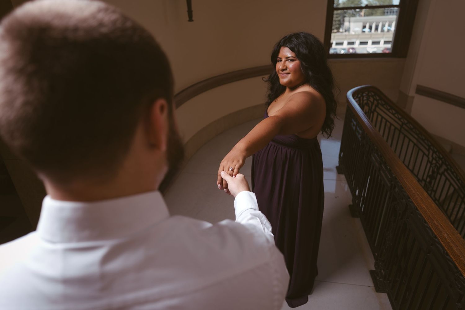Two people share a tender moment near an ornate staircase railing.