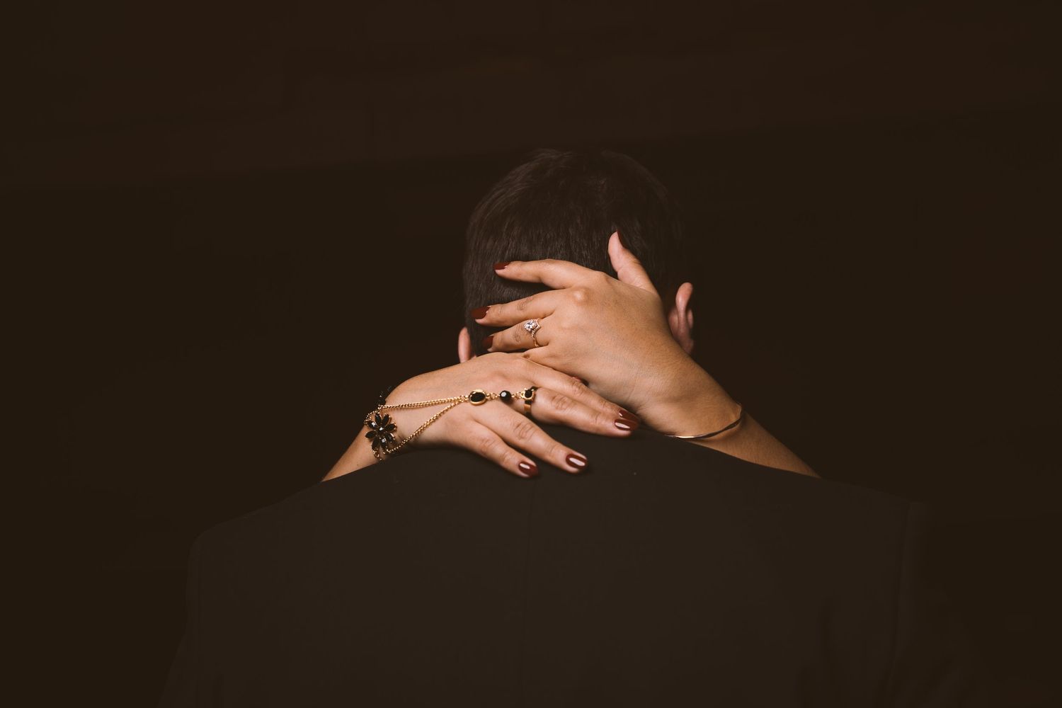 An artistic close-up shot focusing on hands and shoulders in dark lighting.
