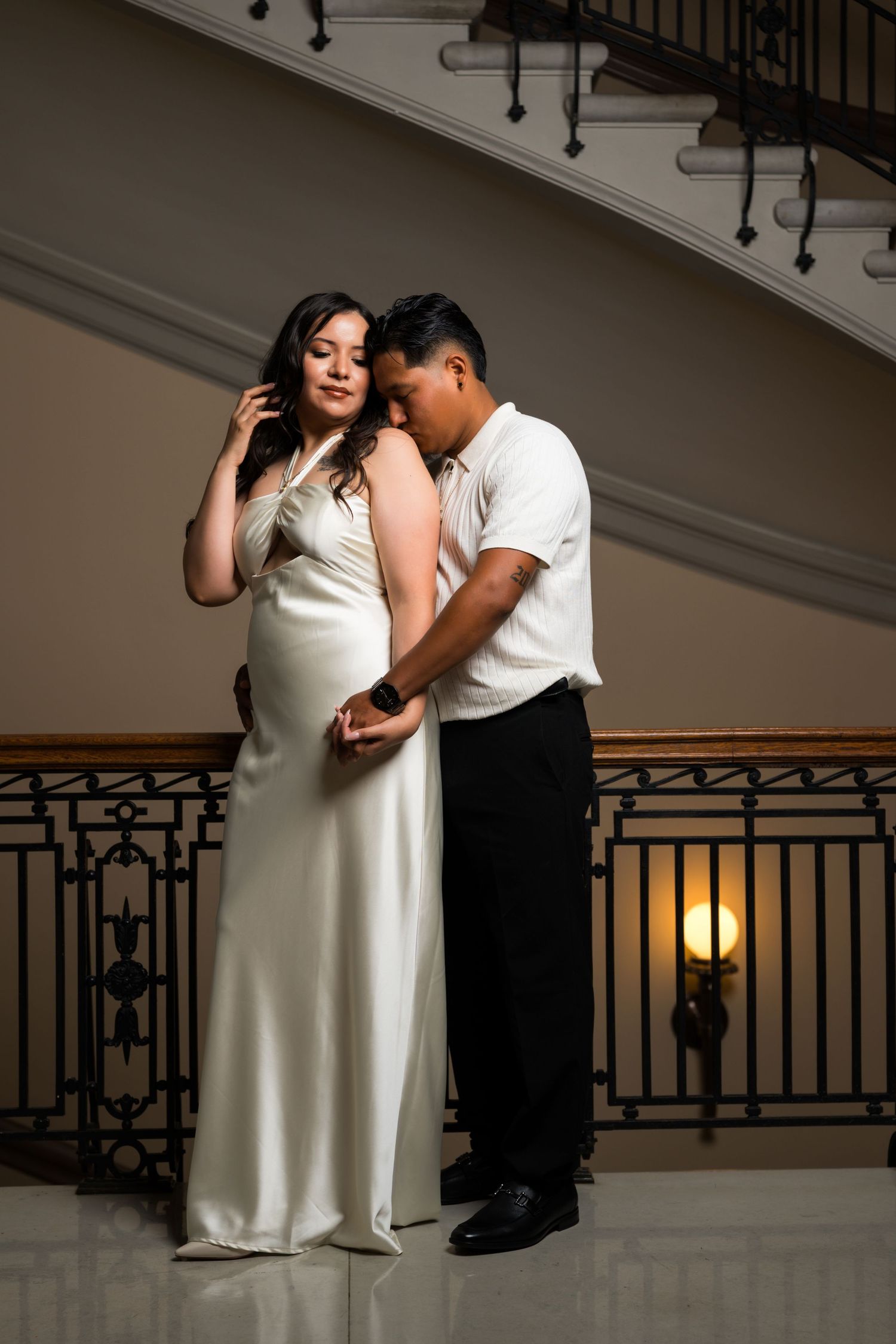 A couple in formal wear dances near an elegant staircase railing.