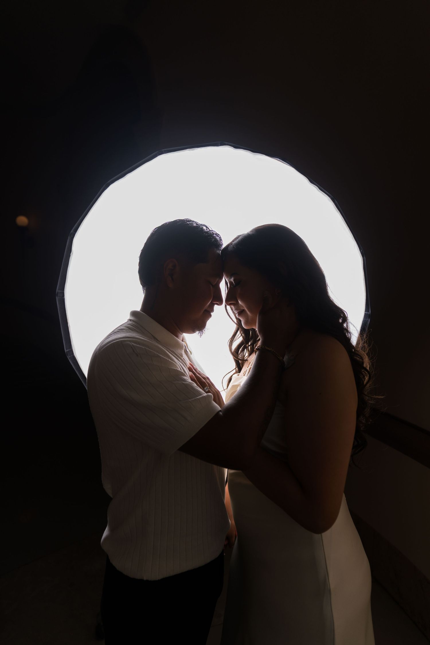 Silhouetted couple shares an intimate moment against a bright backlit background.
