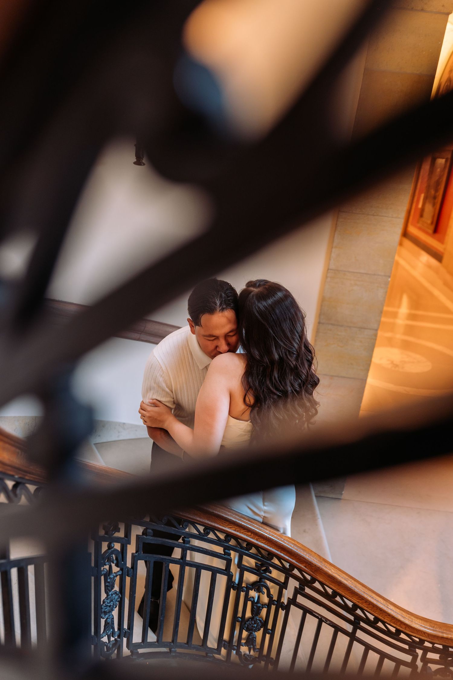 Romantic couple moment captured through decorative staircase railings in warm interior light.