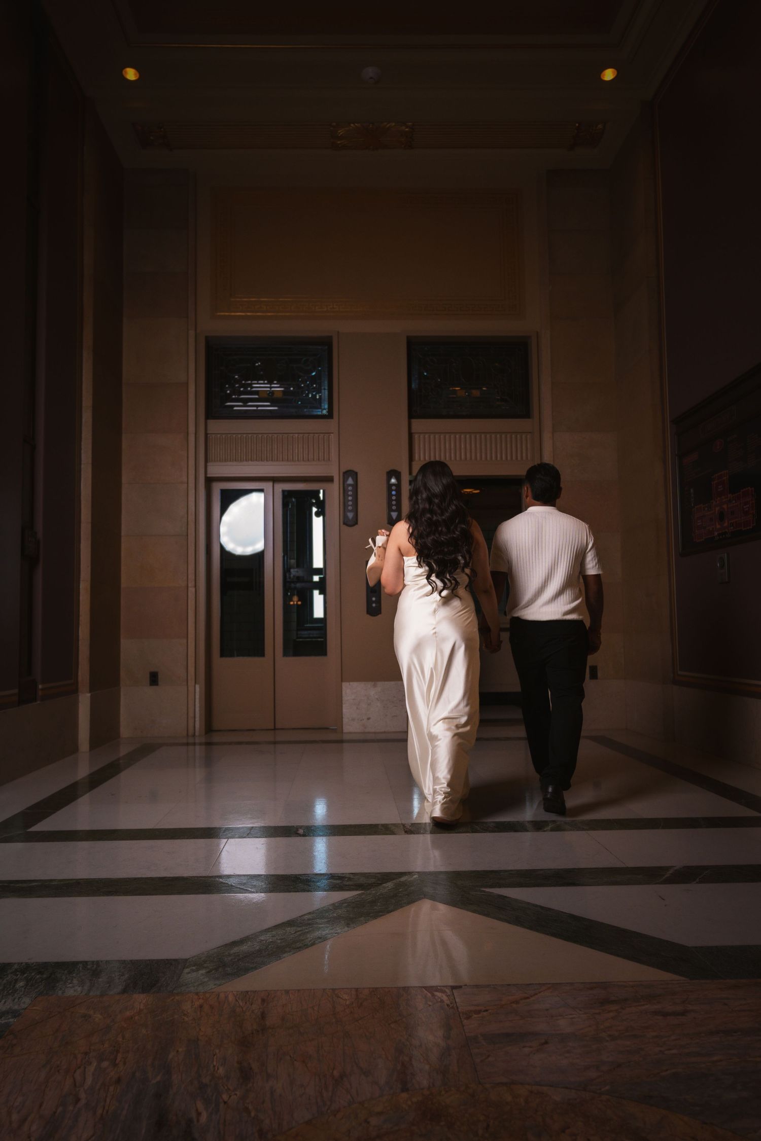 Couple walks through dimly lit grand hallway with marble floors.
