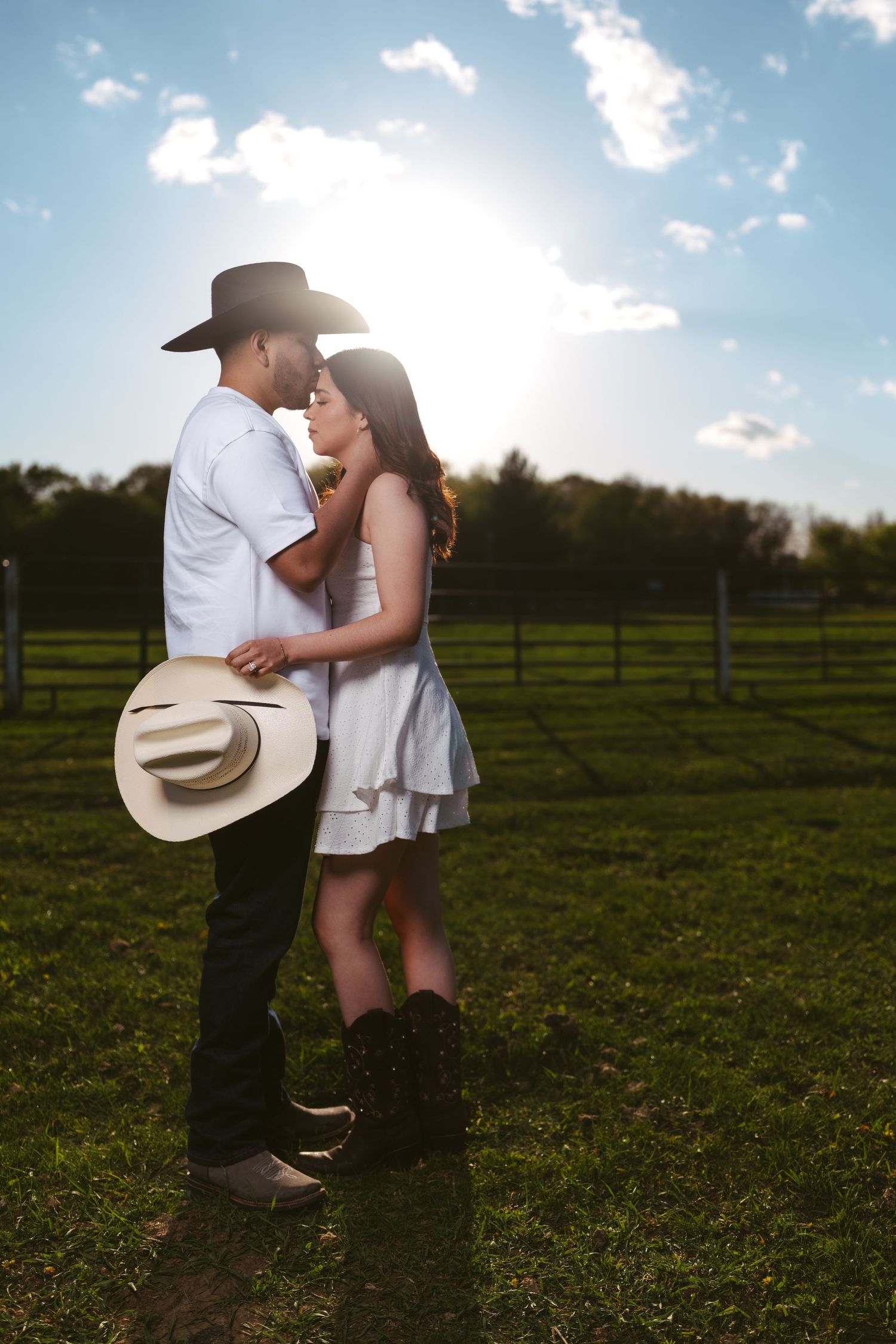 Couple embracing at golden hour in a farm field with cowboy hats.