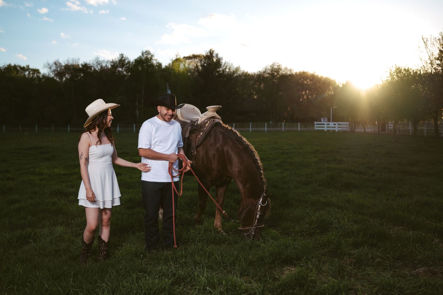 Couple in cowboy hats feeding a brown horse at sunset on a farm.