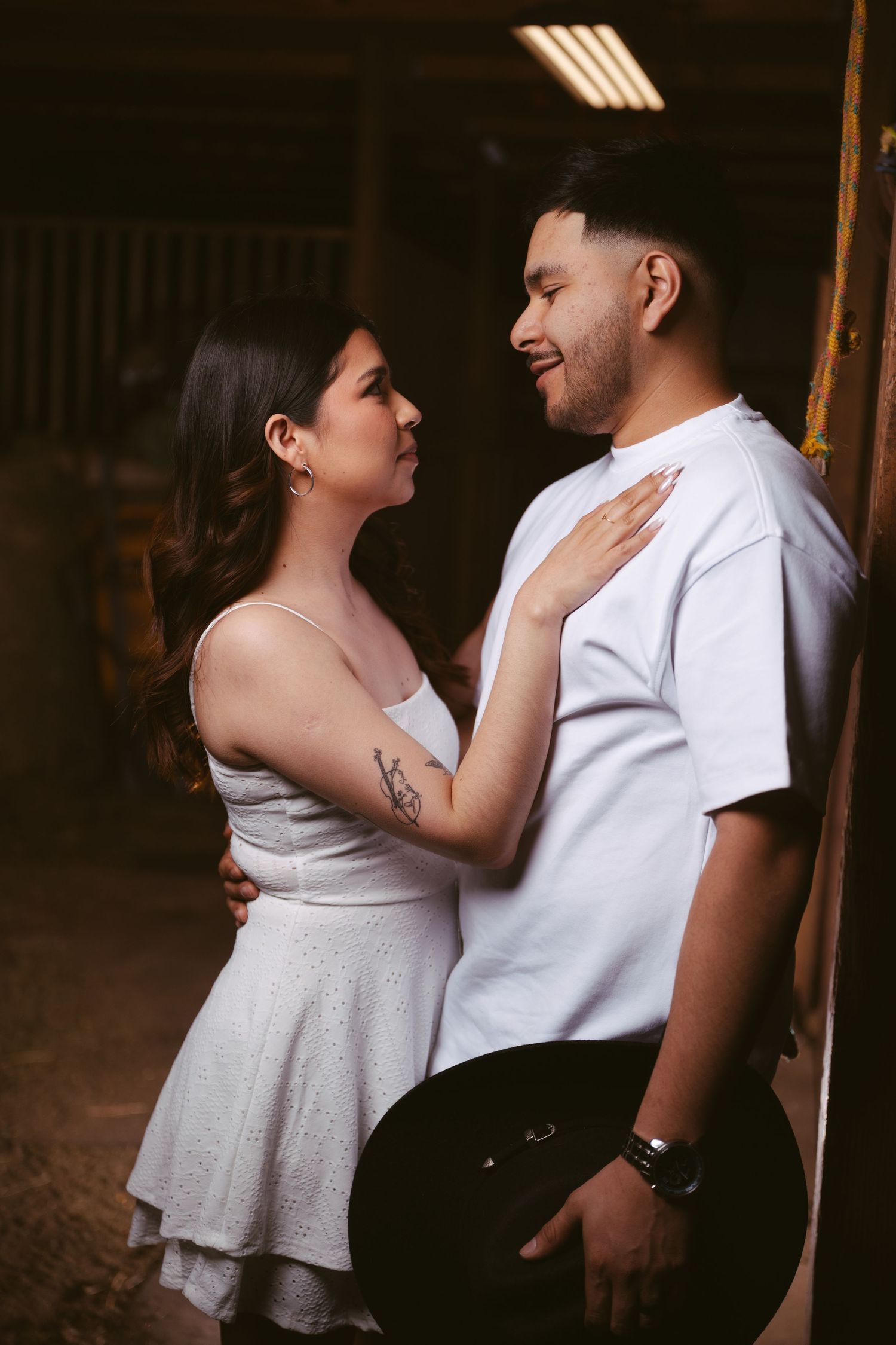 Young couple in white outfits share an intimate moment inside a barn.
