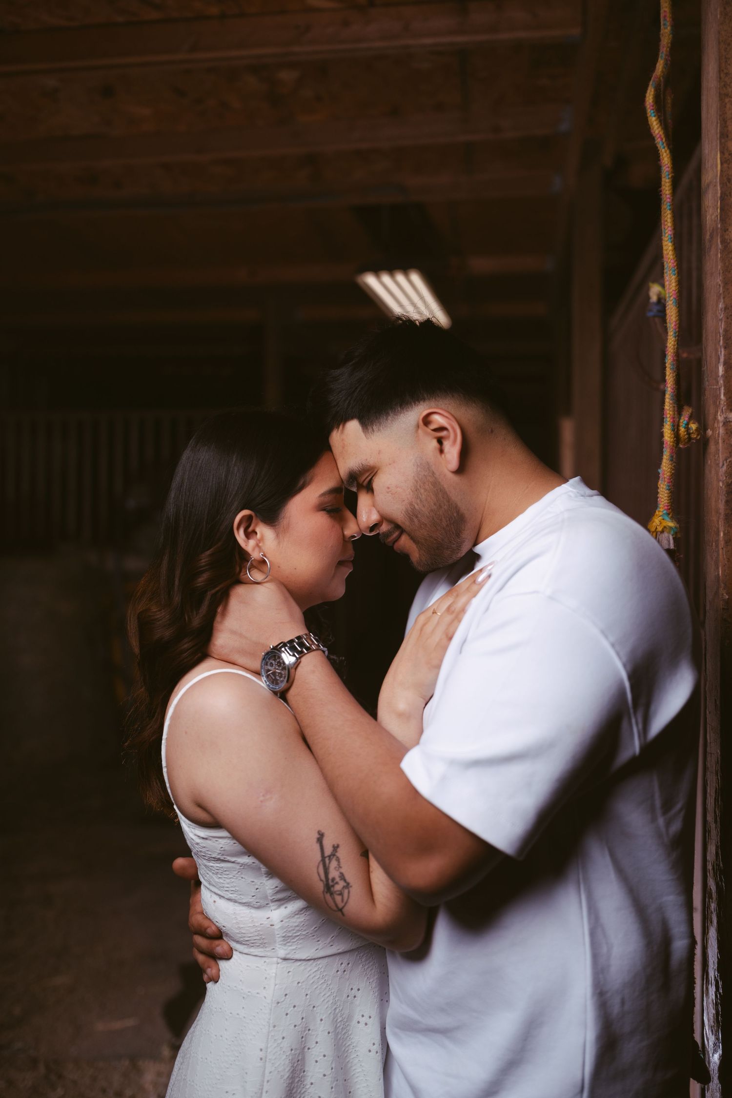 Romantic couple sharing an intimate moment, foreheads touching, inside a rustic barn setting.