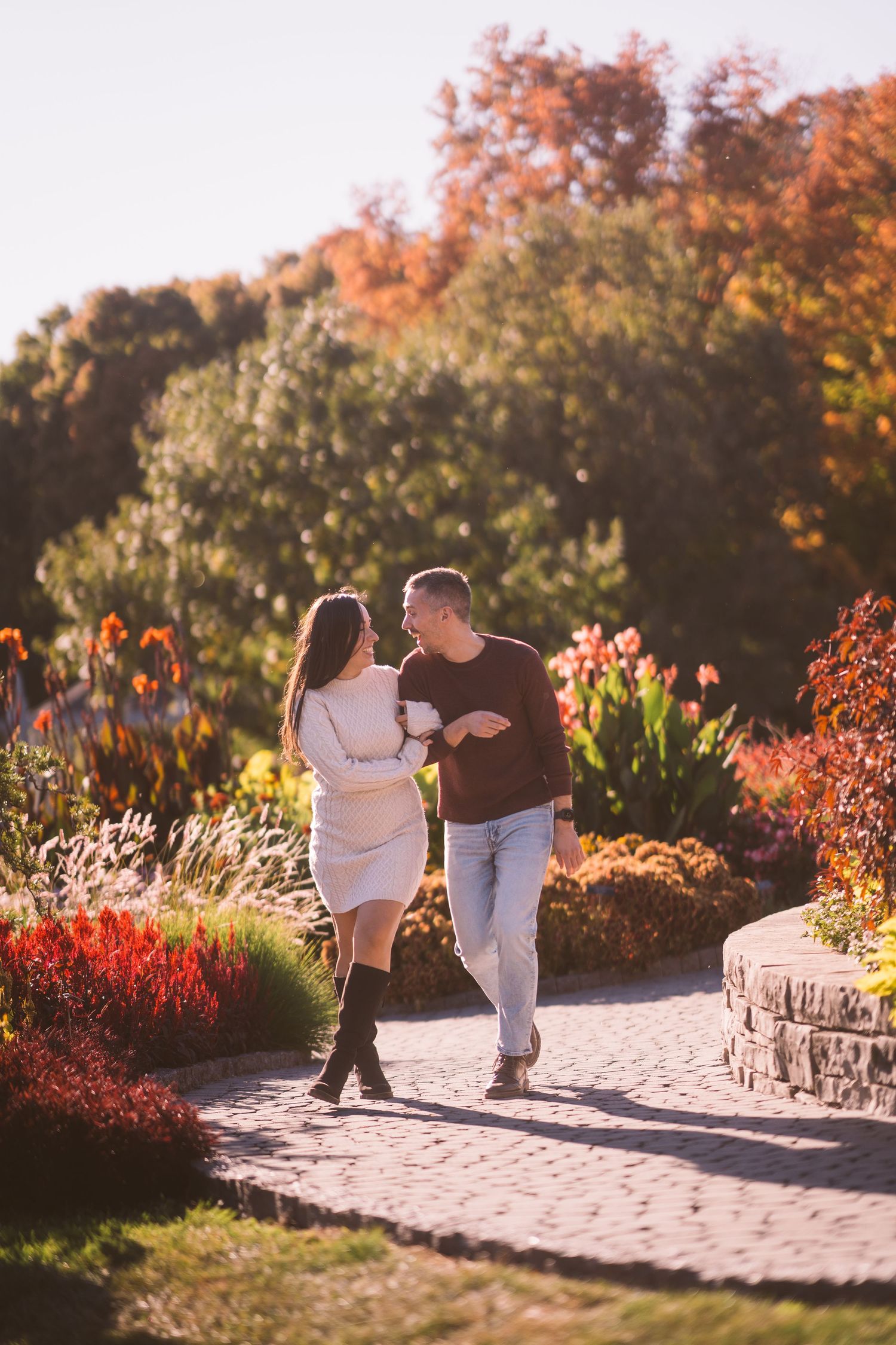 Couple walking along a stone pathway surrounded by vibrant fall flowers and foliage.
