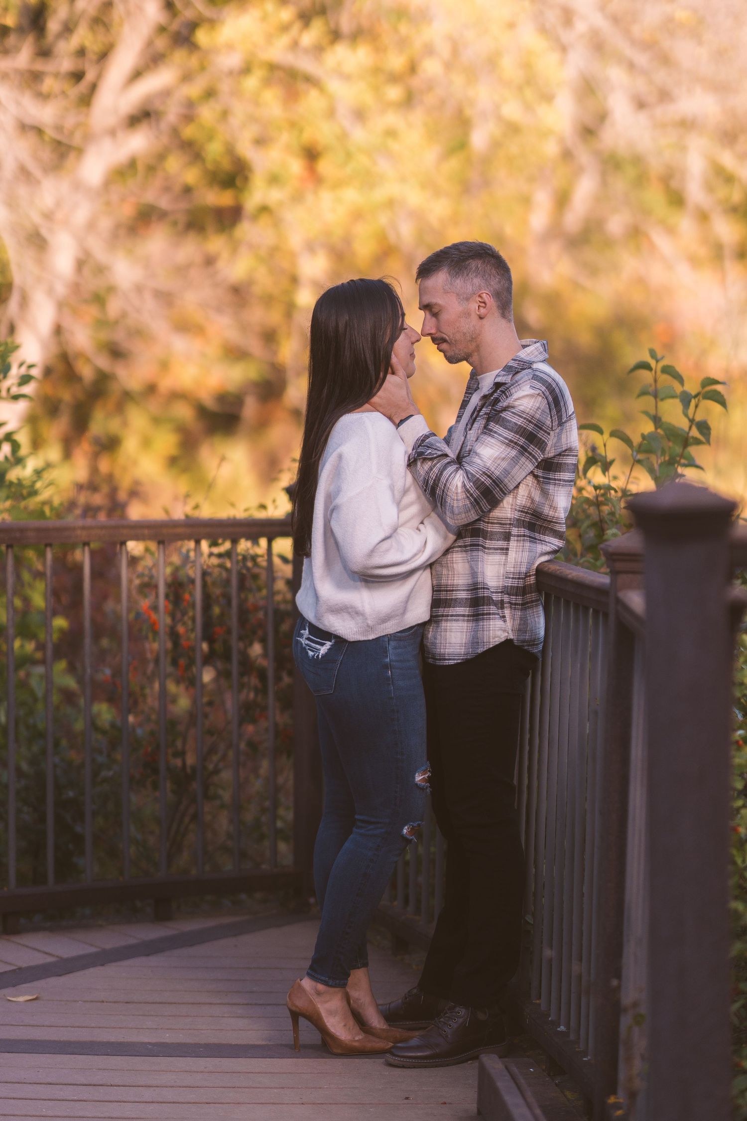 Couple sharing romantic moments on an autumn deck with golden foliage in background.