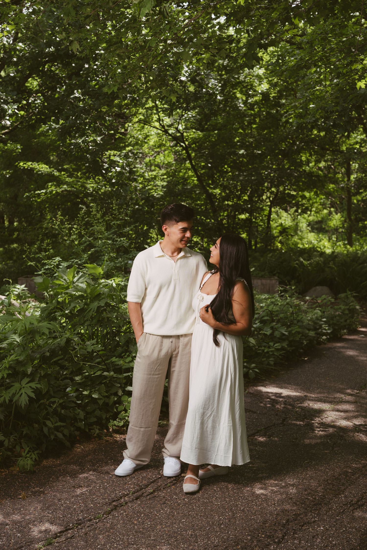 Couple gazing at each other on a shaded garden path surrounded by vibrant green foliage.