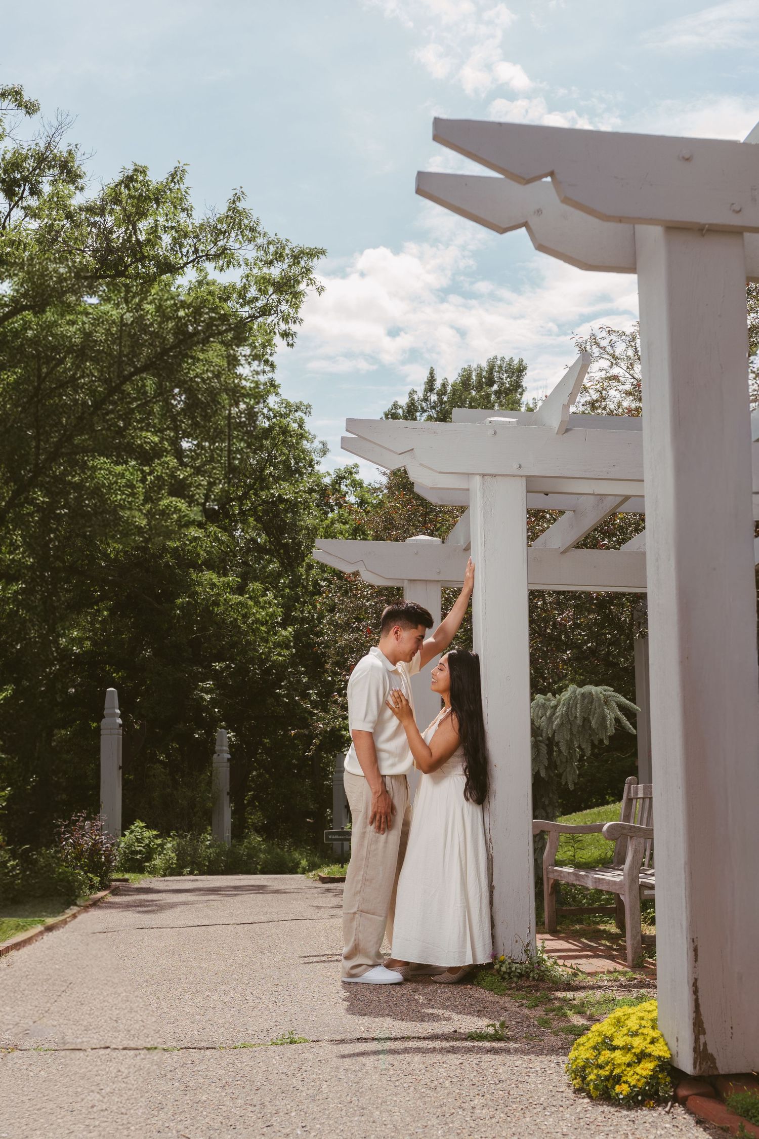 Romantic couple sharing a kiss under a white pergola in a sunny park garden.