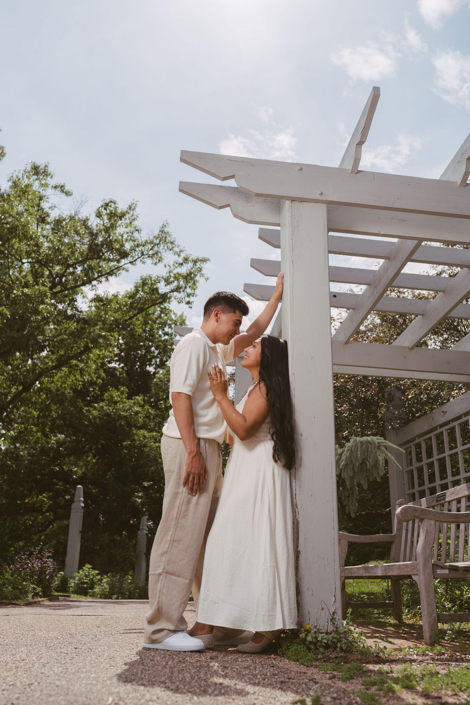 Couple sharing a tender kiss under a white pergola in a sunny garden setting.