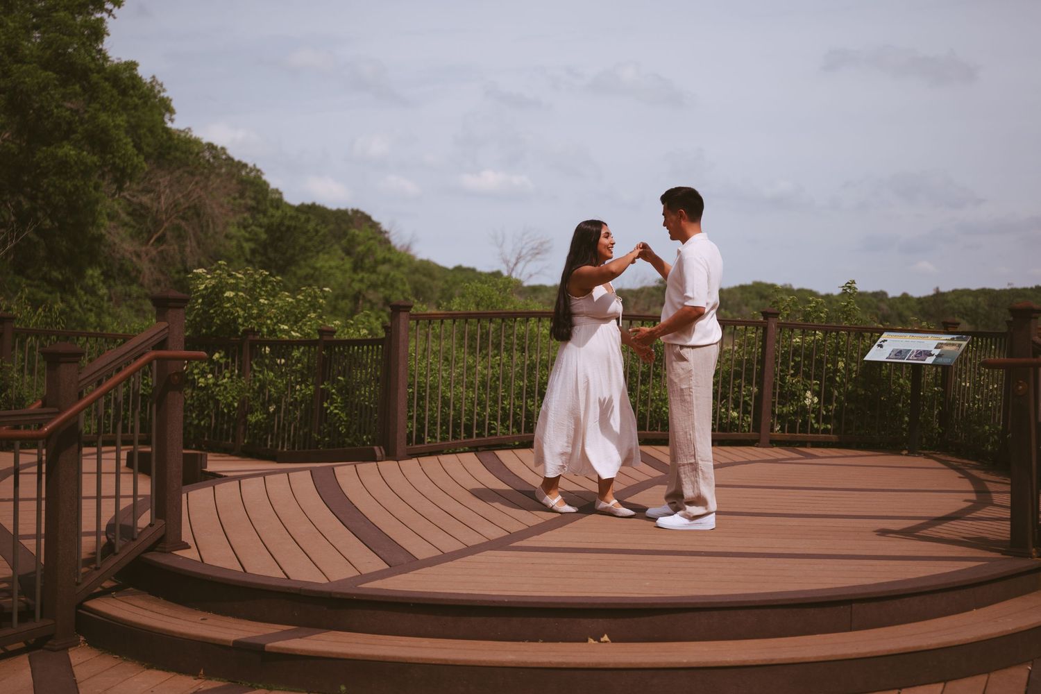 Couple in white outfits dancing on a wooden deck overlook surrounded by lush tropical greenery.