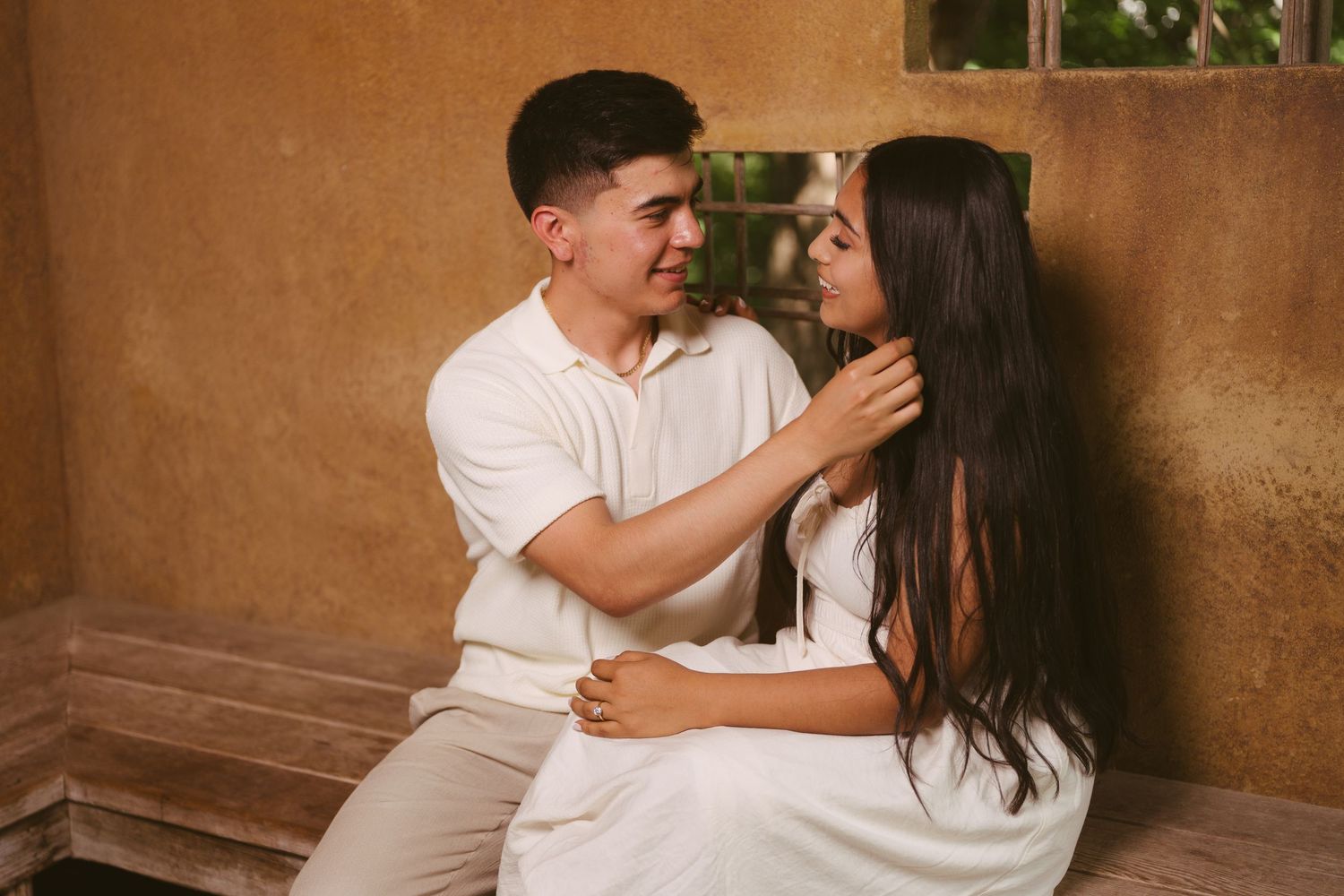Romantic couple sitting together against a warm terracotta wall, man gently touching womans face.