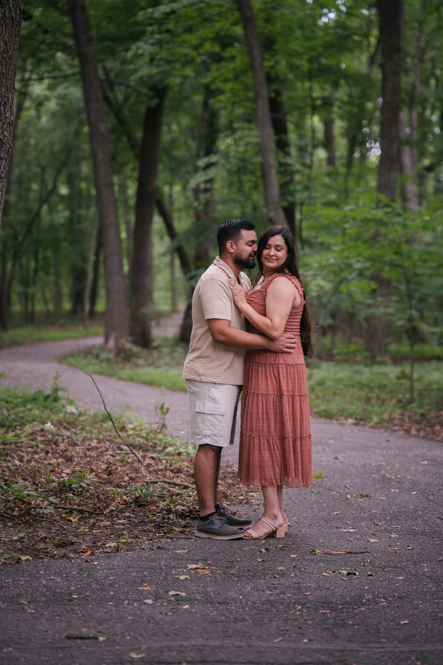 A couple in matching outfits shares a tender moment on a forest path.