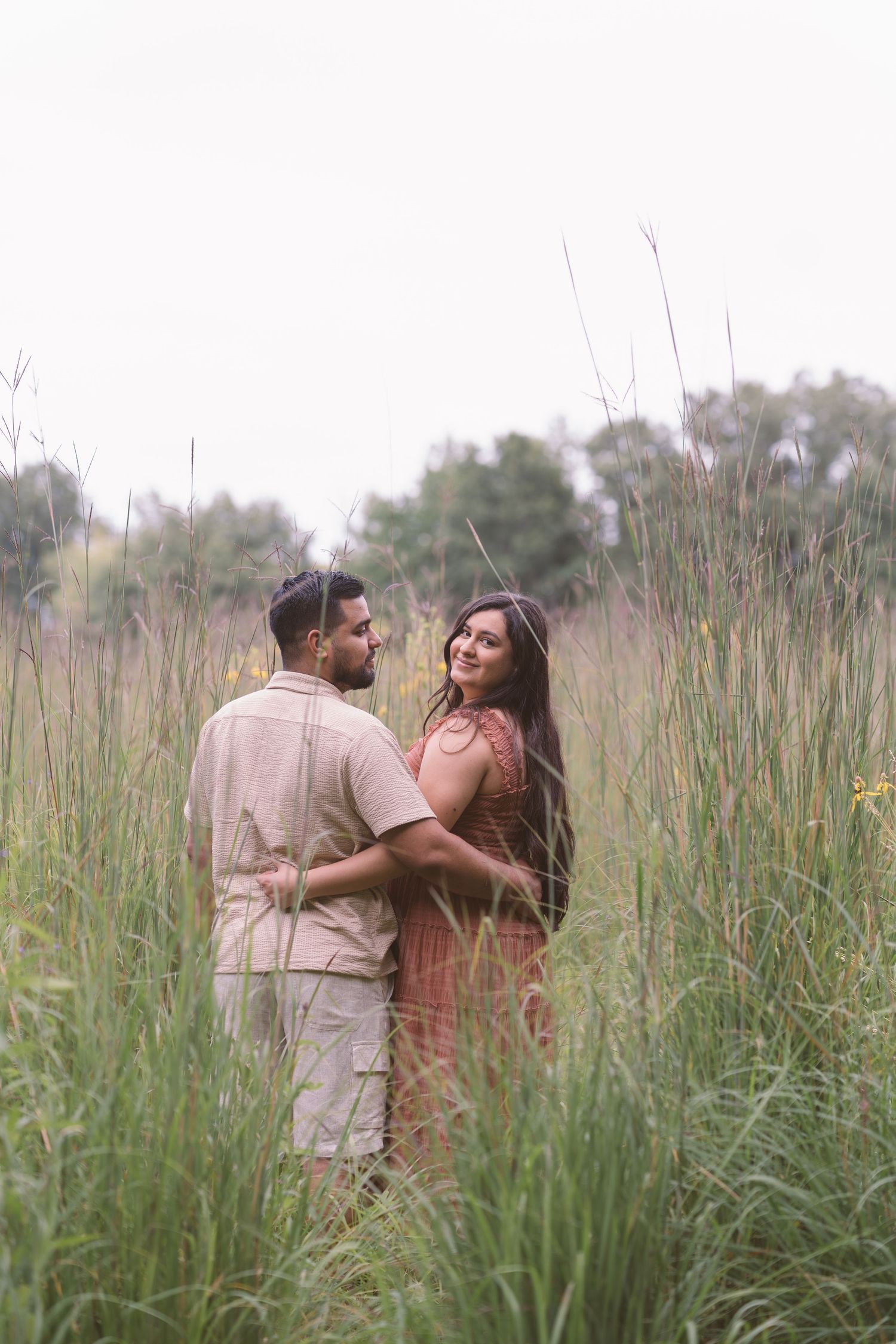 Couple embraces in tall grass during a romantic outdoor photoshoot.
