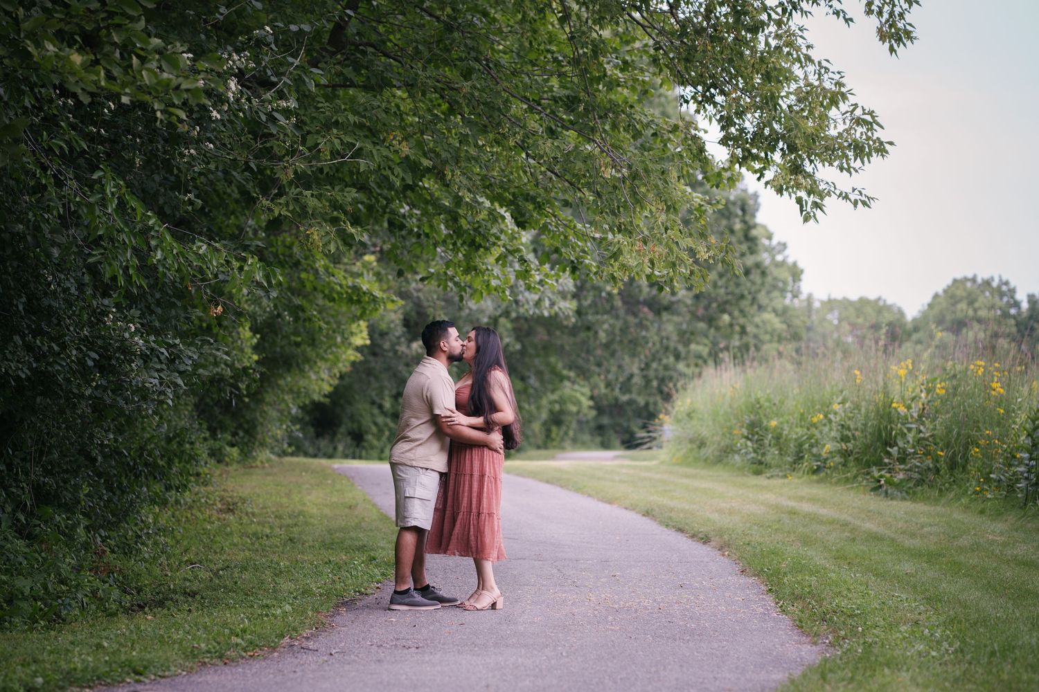 A couple in coordinated outfits shares a moment on a paved nature trail.