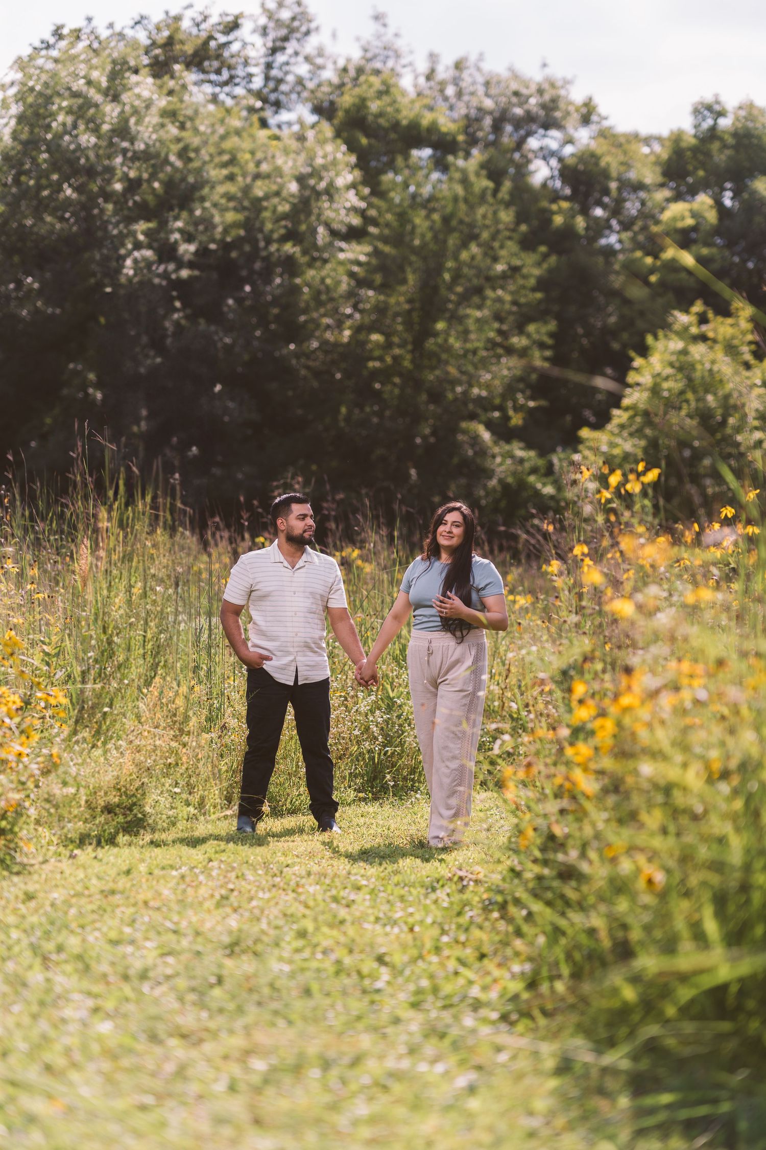 Couple holds hands while walking through a wildflower meadow on a sunny day.