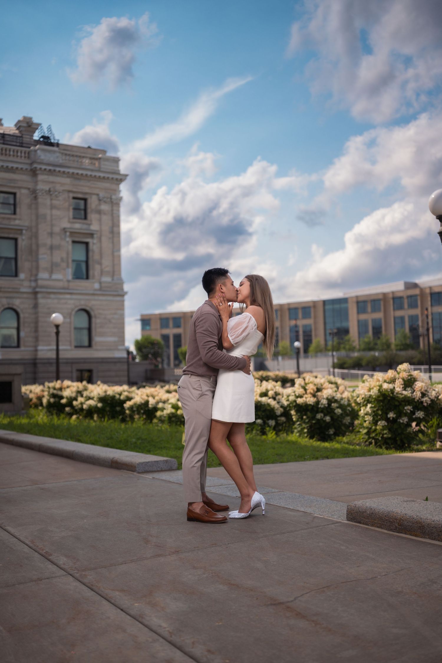 Engagement photos taken outside a historic building with blooming flowers and blue skies.