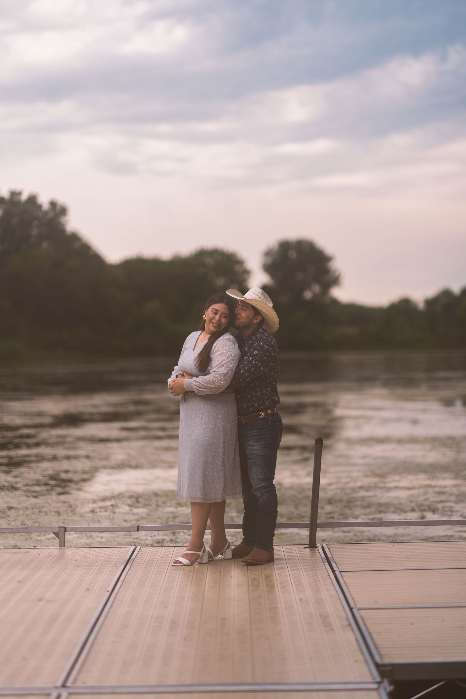 A couple shares an intimate moment on a wooden dock at sunset.