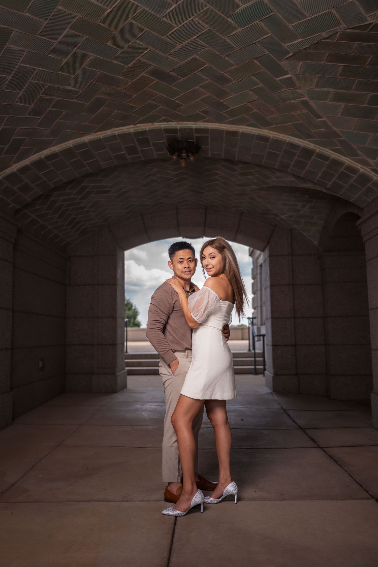 Couple poses under a brick archway during an urban photoshoot.