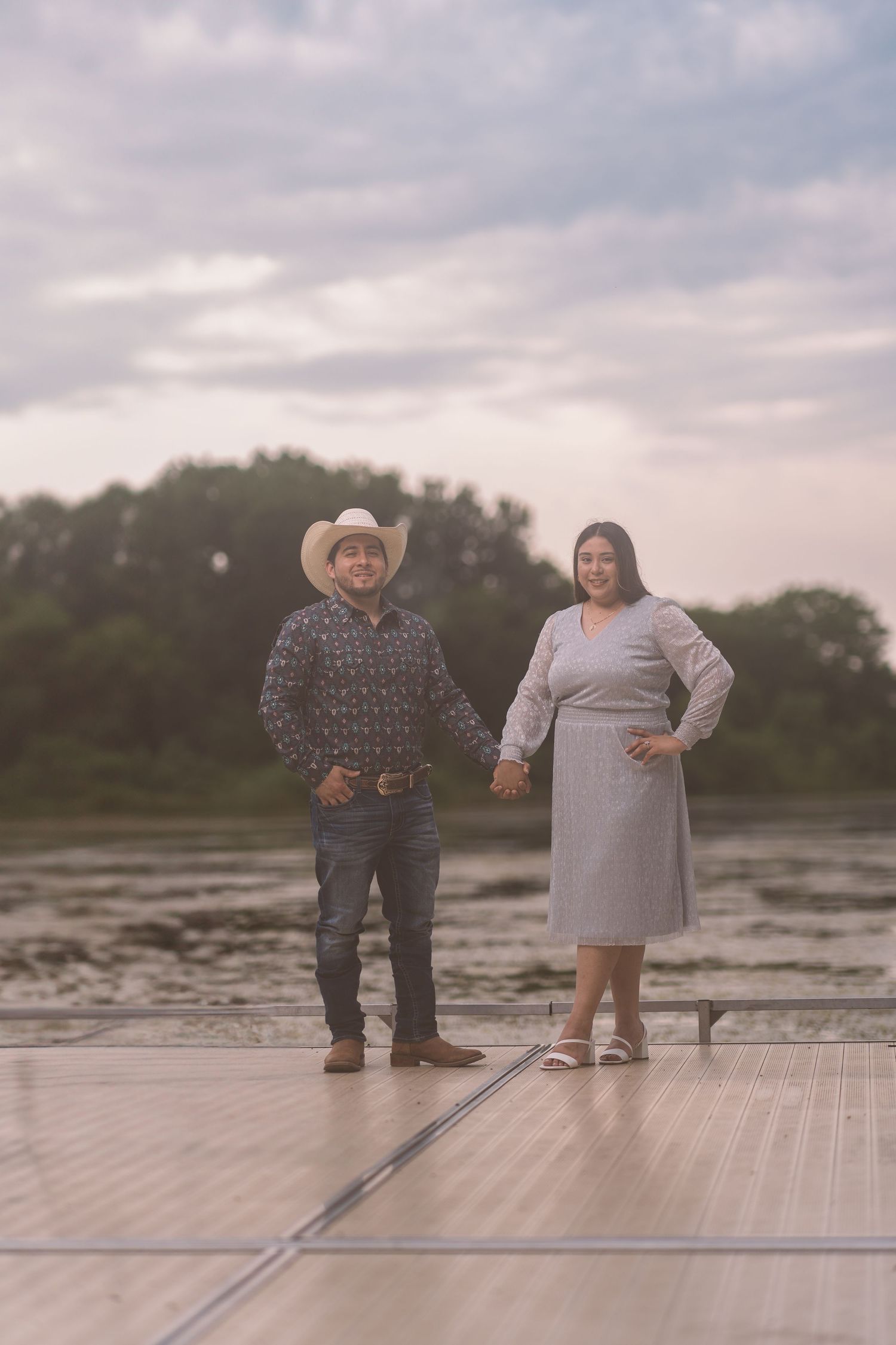 A couple in western attire stands together on a rustic dock.