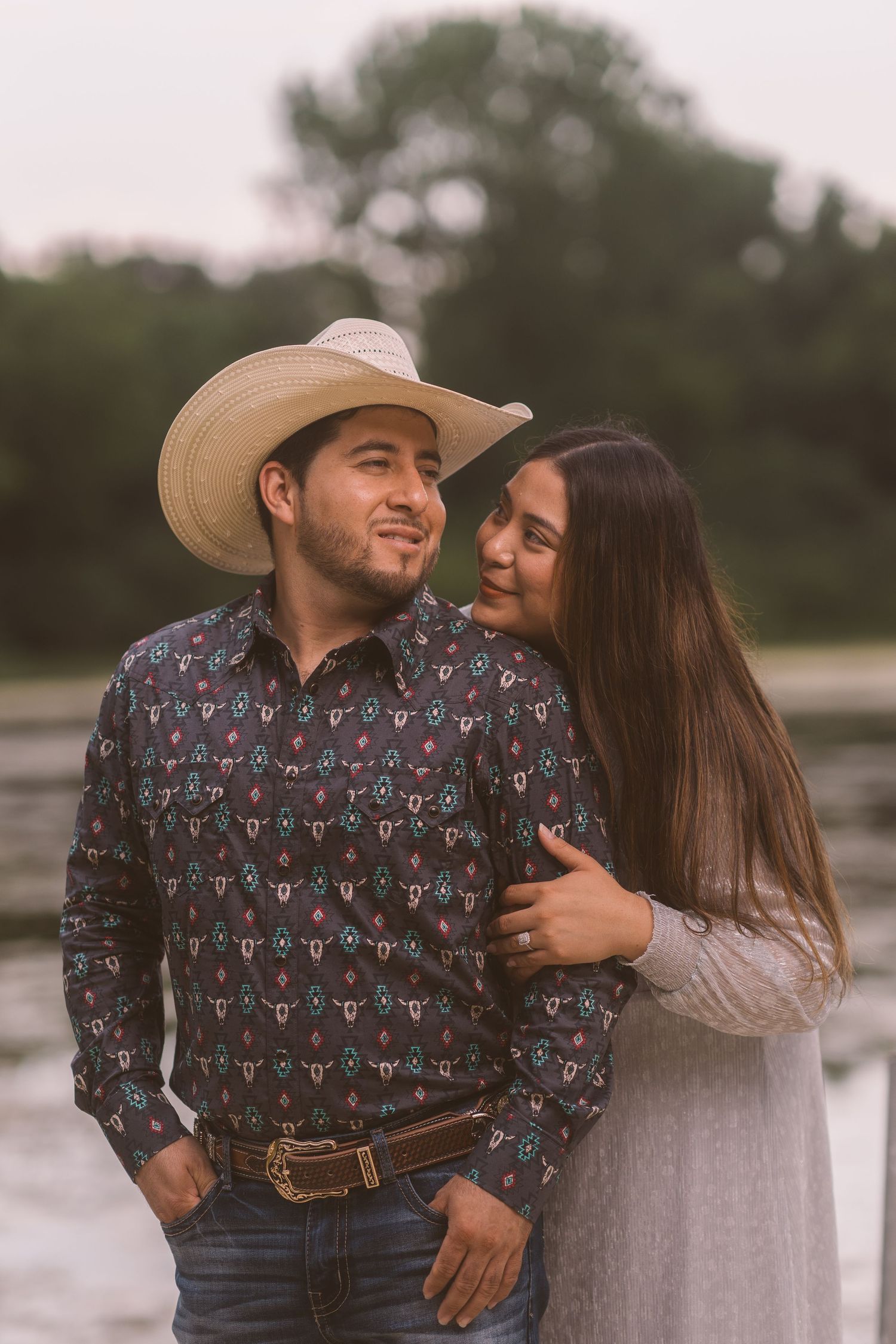 A couple in western wear shares a romantic moment outdoors.