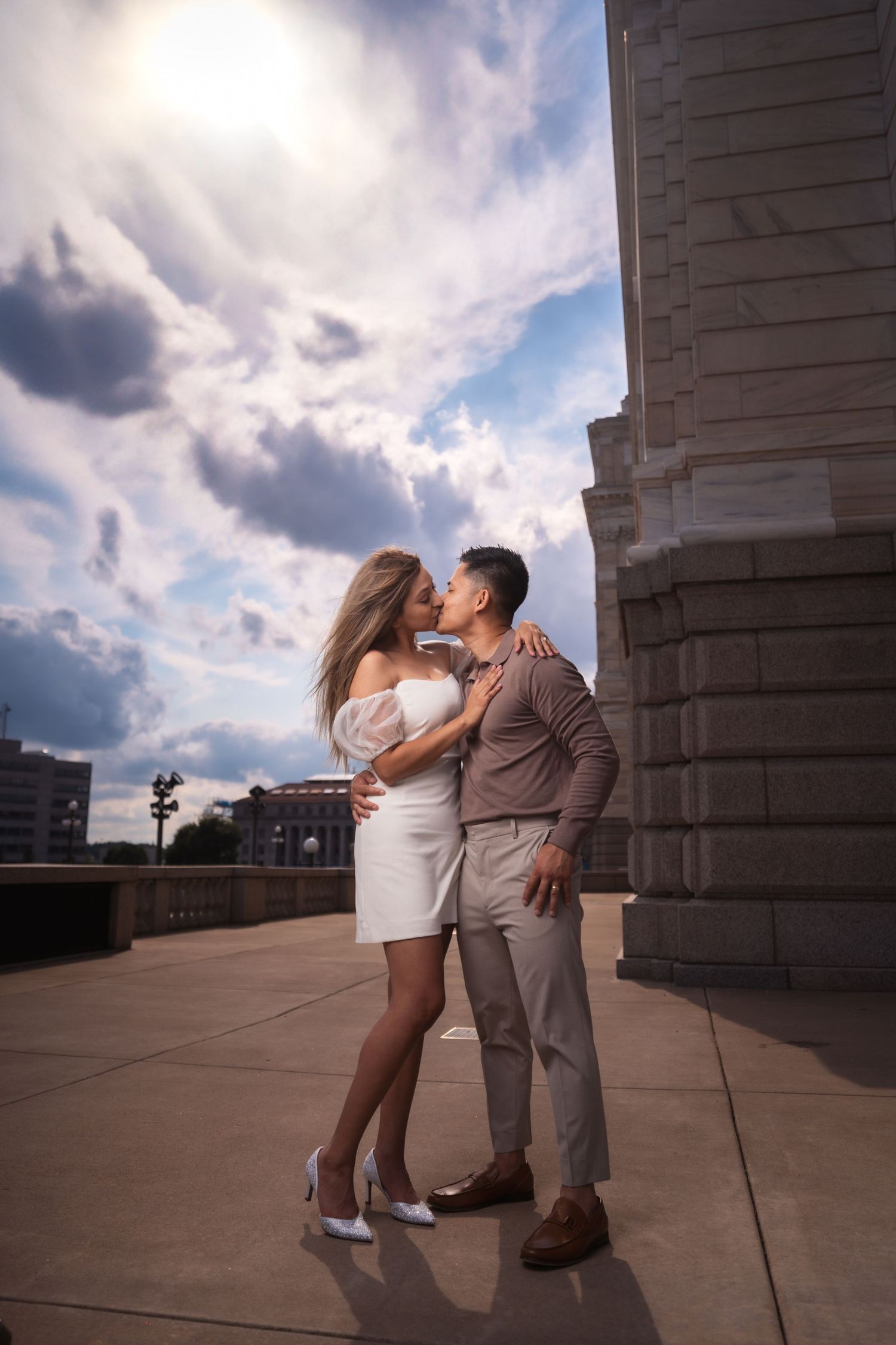 Romantic moment captured against dramatic clouds and classical architecture.