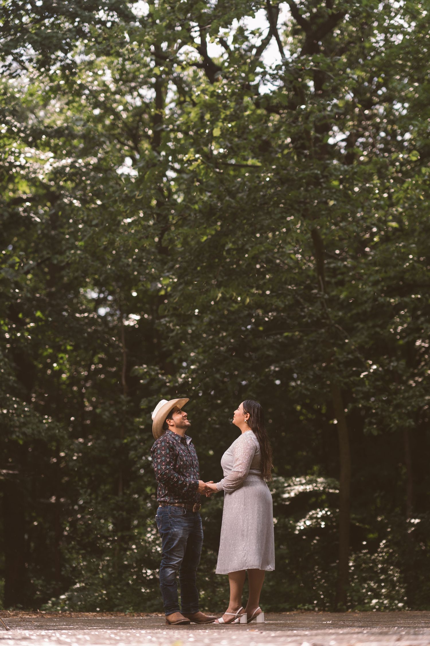 A couple dances together under green trees in a park.